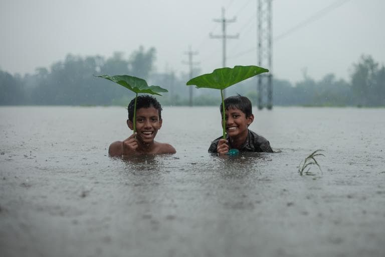 A wide-angle photo of monsoon clouds over green paddy fields in India, with farmers working, dramatic sky.