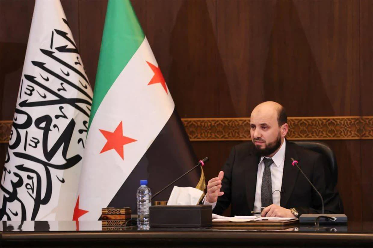 Syrian interim leader speaks at a press conference beside national flag, addressing governance issues and upcoming elections.