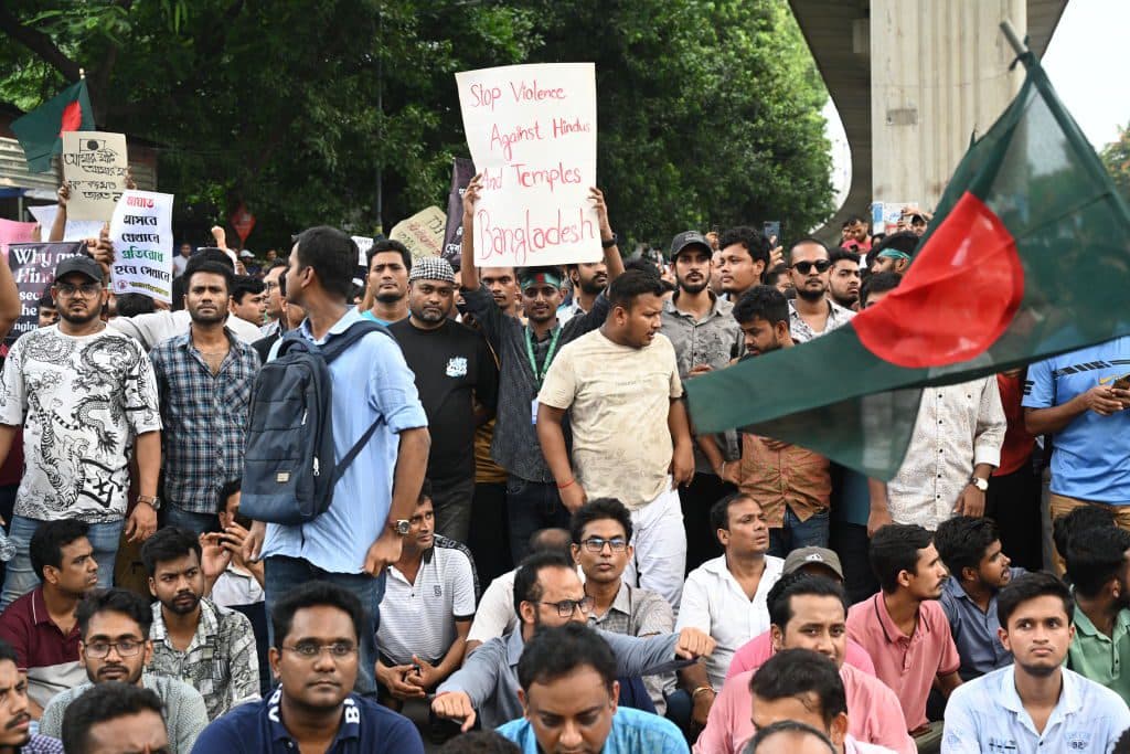 People protest in Bangladesh holding signs and flags, demanding an end to violence against Hindus and attacks on temples.