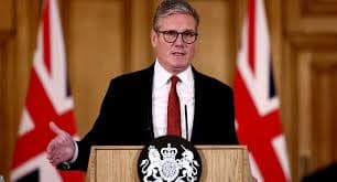 A political leader delivering a formal address at a government press brief, standing at a podium with the official UK emblem