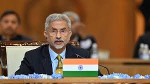 Indian External Affairs Minister addressing an international forum, seated behind the Indian national flag.