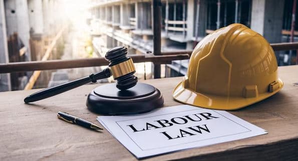 A gavel, safety helmet, and document titled “Labour Law” on a desk, symbolising workers’ rights and labour reforms in India.